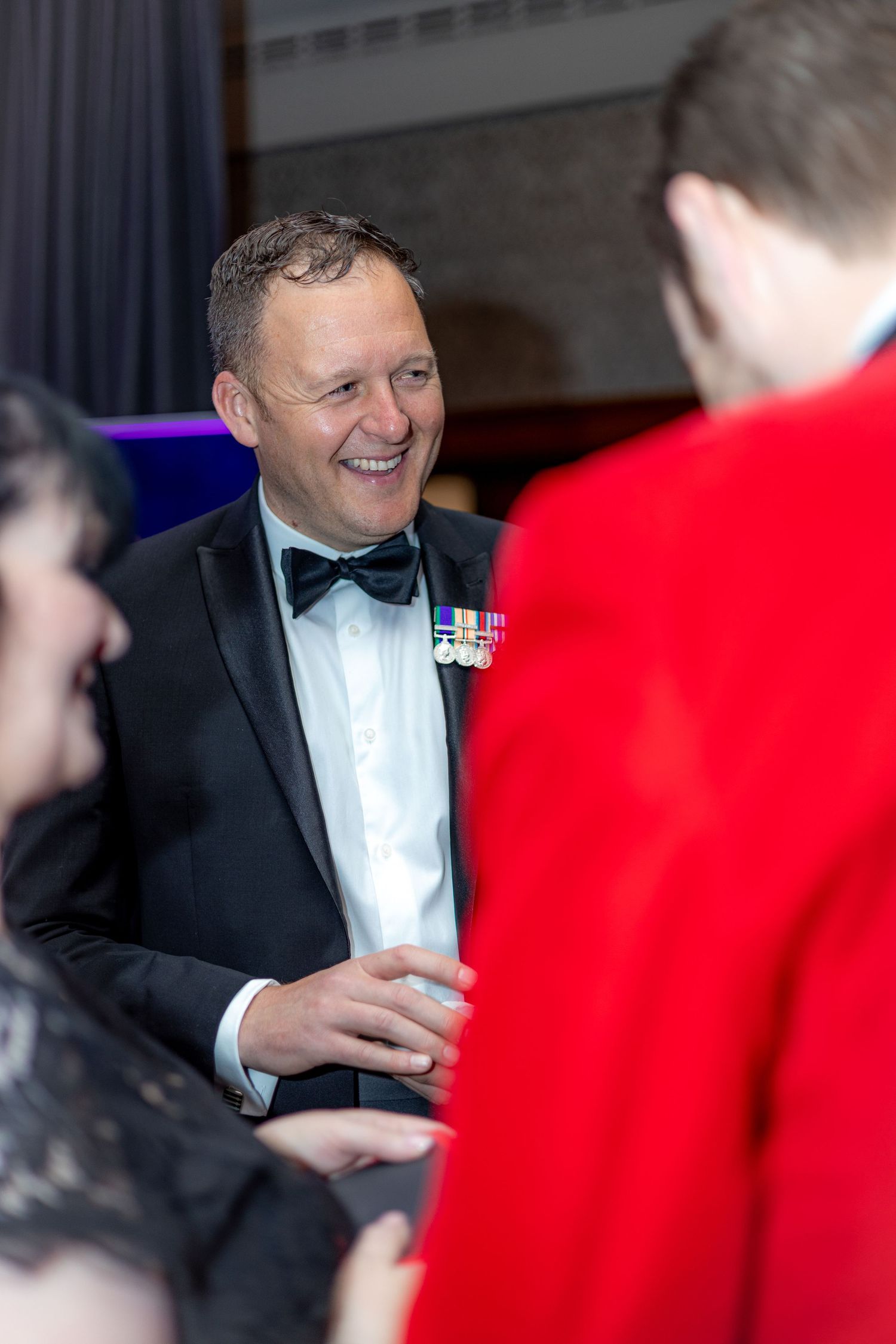 A magician in formal wear performs close-up tricks for party guests.