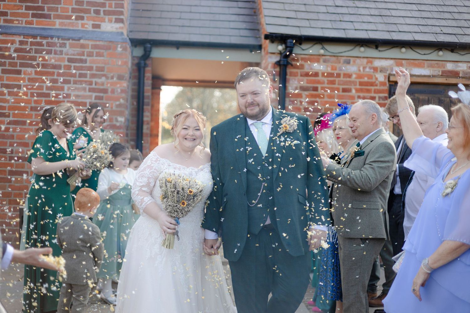 Wedding party celebrates with confetti outside a rustic brick building.