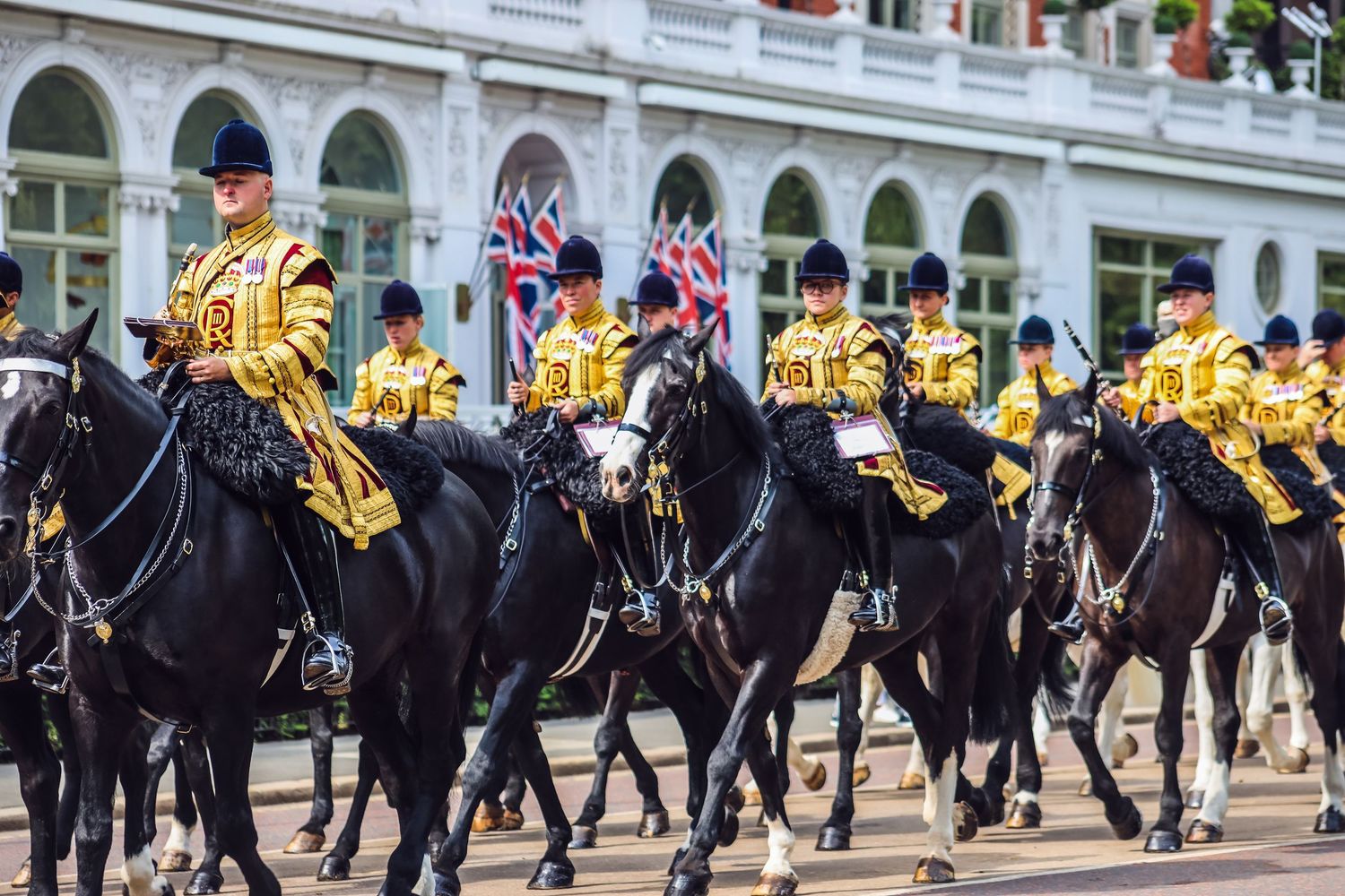Mounted cavalry unit in ceremonial dress marching in formation during a formal parade.