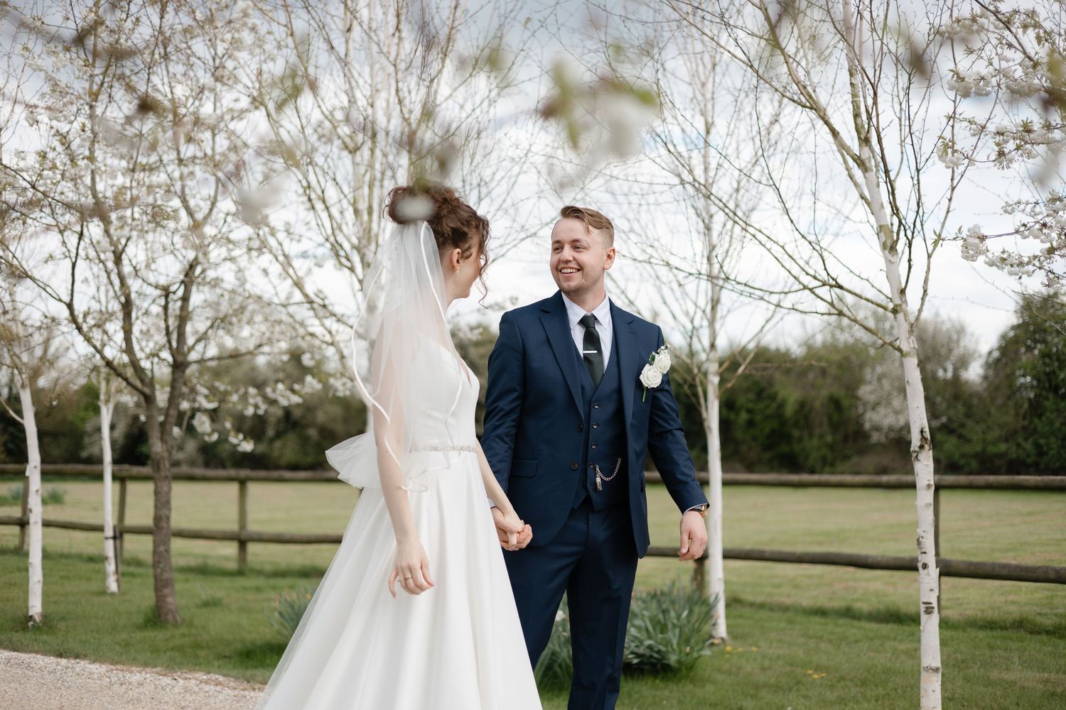 Joyful wedding couple sharing laughs while walking through avenue of white-barked trees.