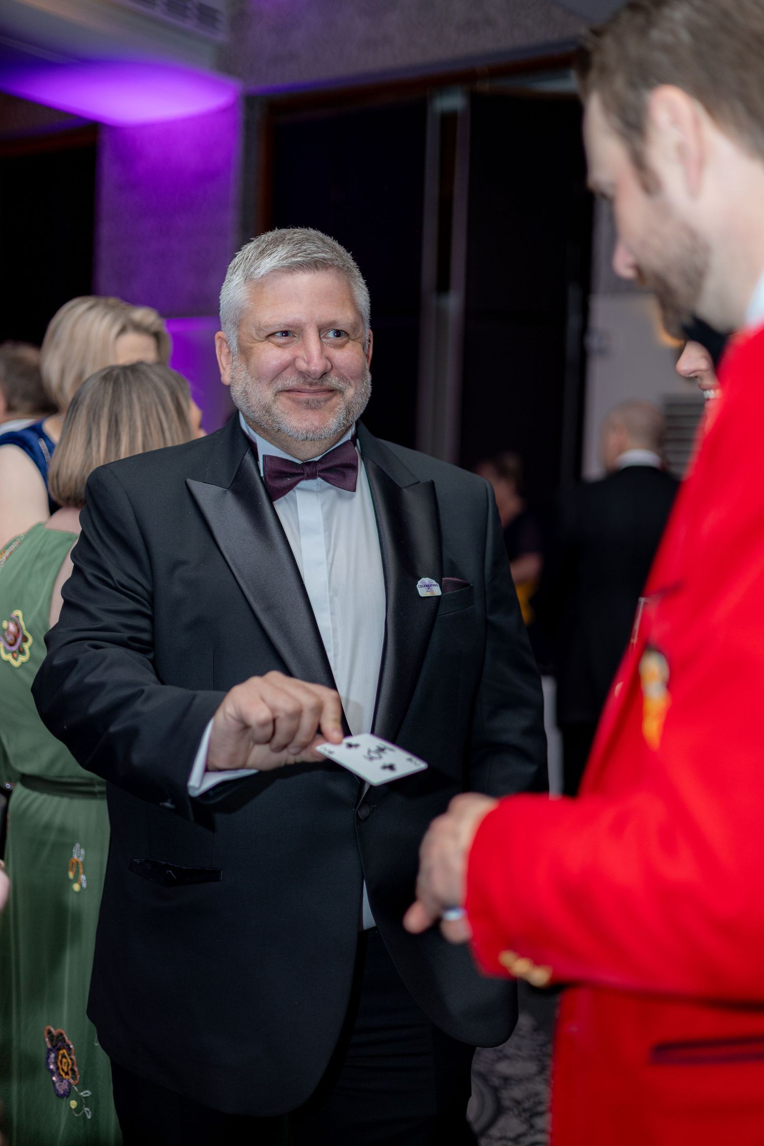 Attendees in formal attire mingling at an evening event with purple lighting.