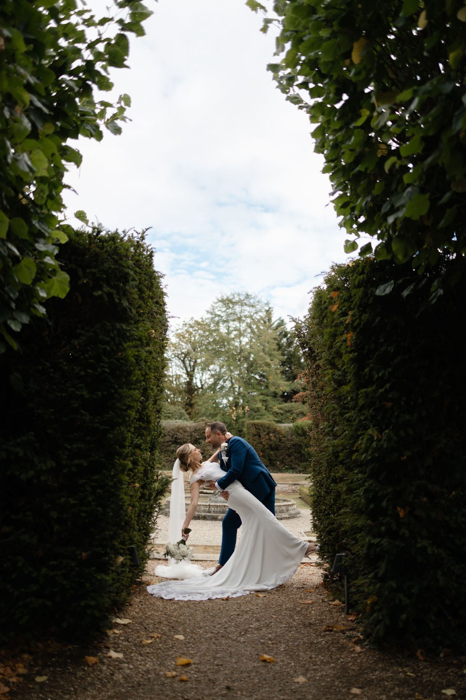 Wedding couple sharing intimate moment in garden path framed by tall hedges.