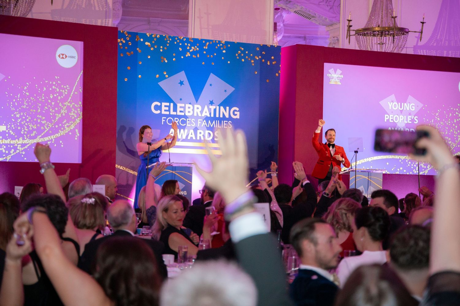 Audience members enjoying an awards ceremony with celebratory graphics displayed on screens.