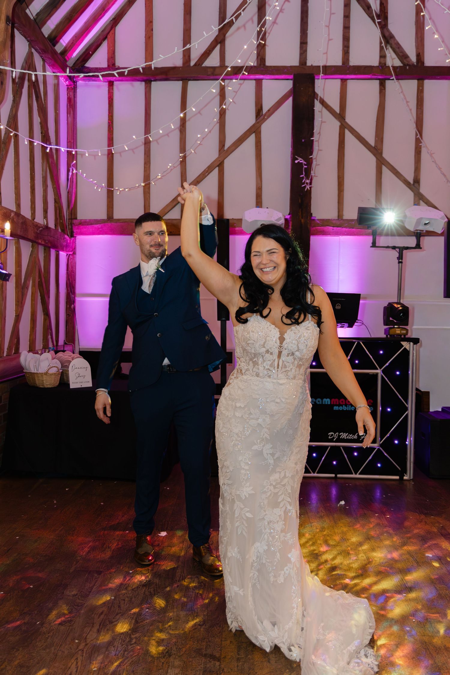 Wedding reception in a barn venue with string lights and pink uplighting creating a festive atmosphere.