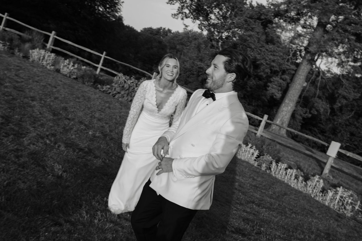 Black and white photo of a bride and groom holding hands while walking outdoors on their wedding day.