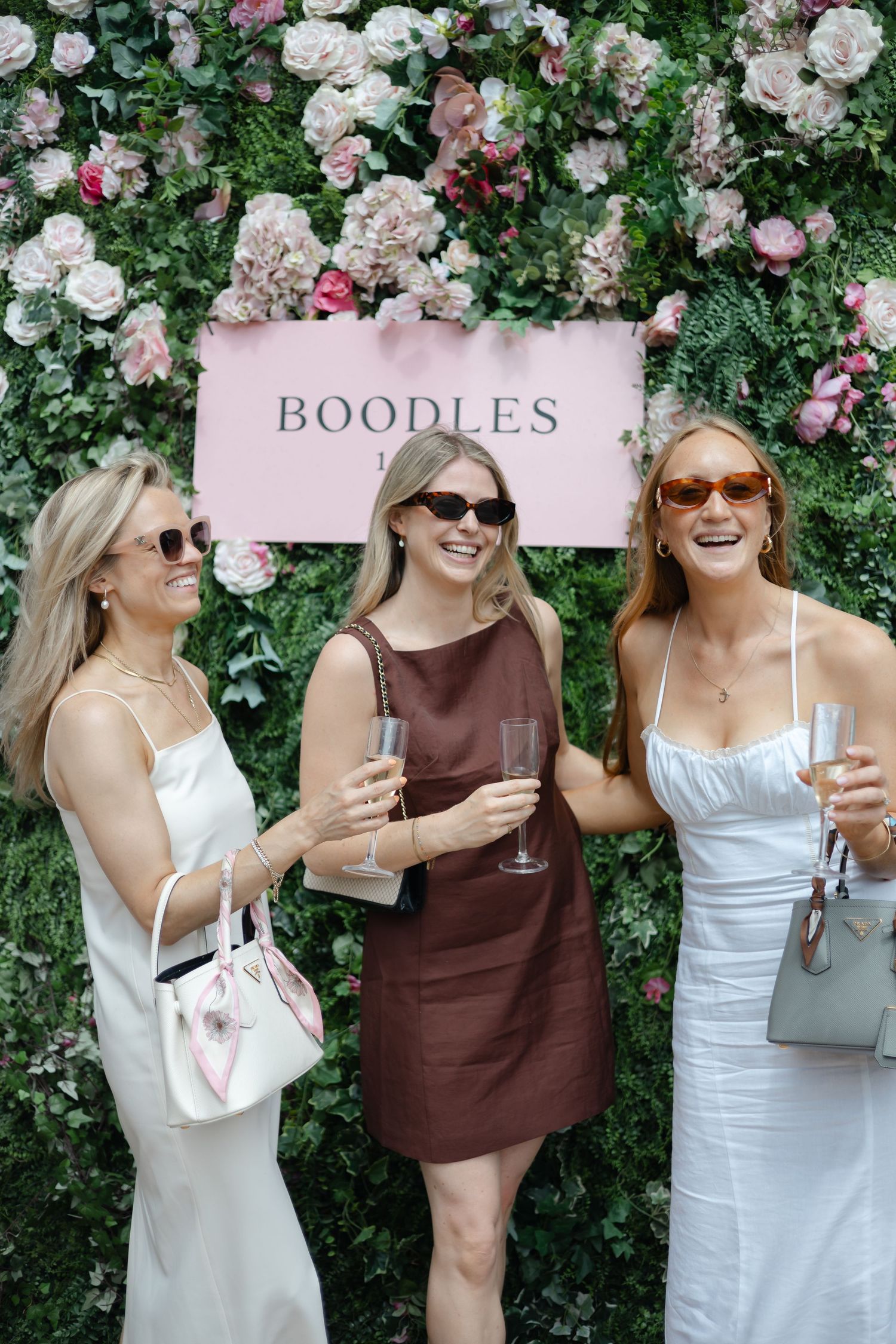 Friends enjoying drinks in front of floral wall at summer garden party.