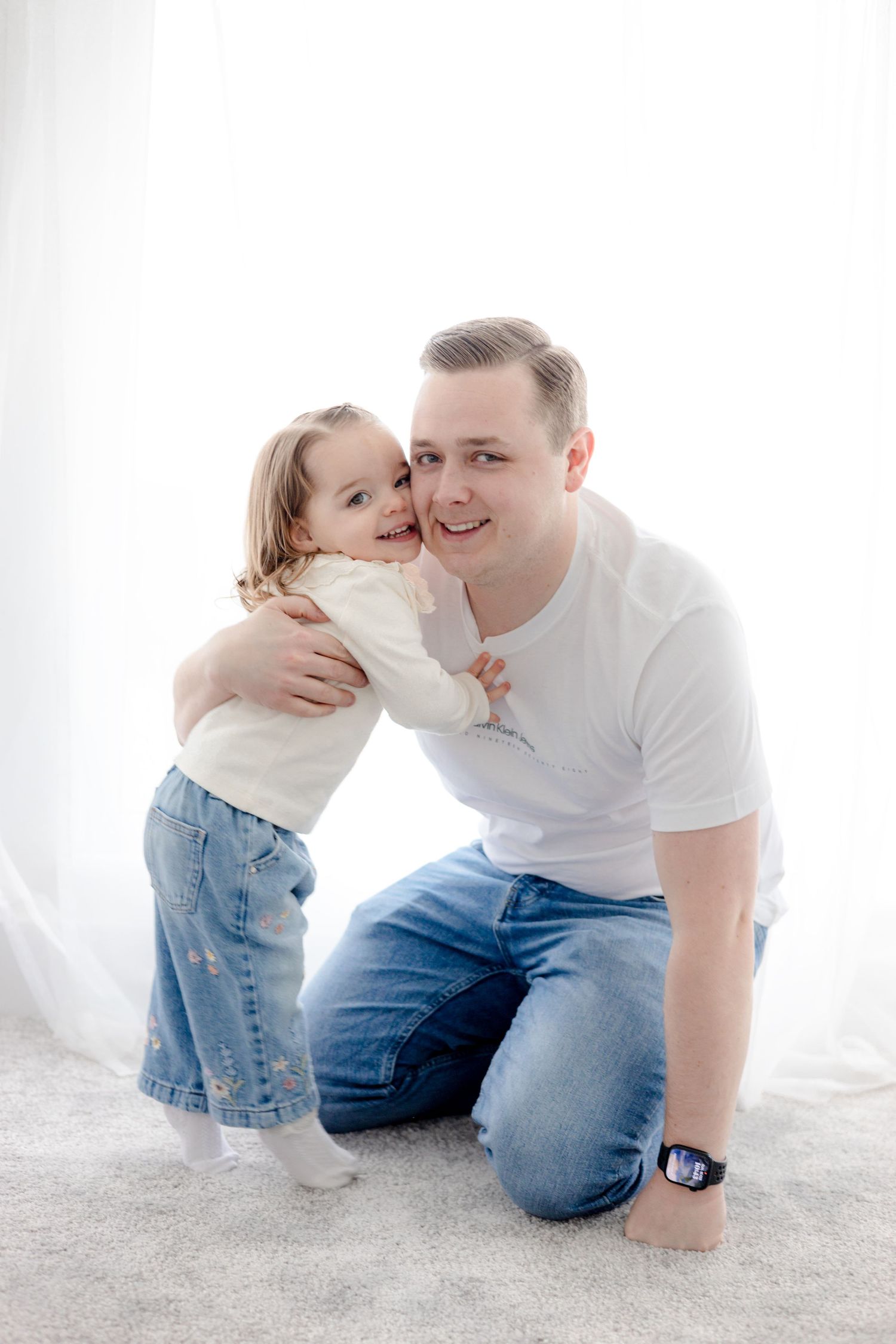 Family playing and laughing together on white carpet in bright room.