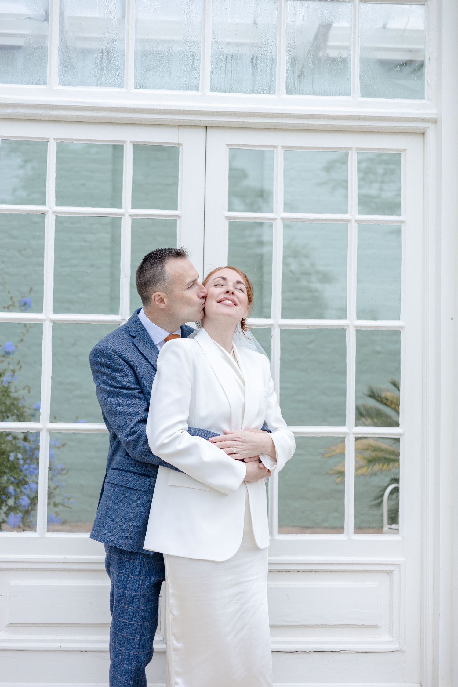 Romantic couple moment captured against white window panes of classic building.
