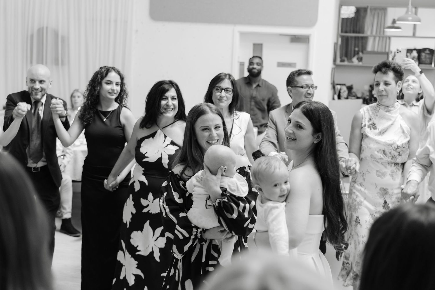 Wedding guests dance and celebrate together in a reception hall with white curtained walls.
