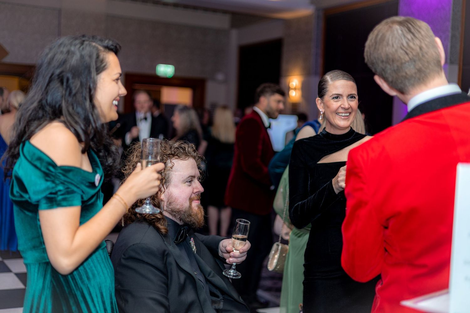 People enjoying conversation at a formal event with festive red and green attire.