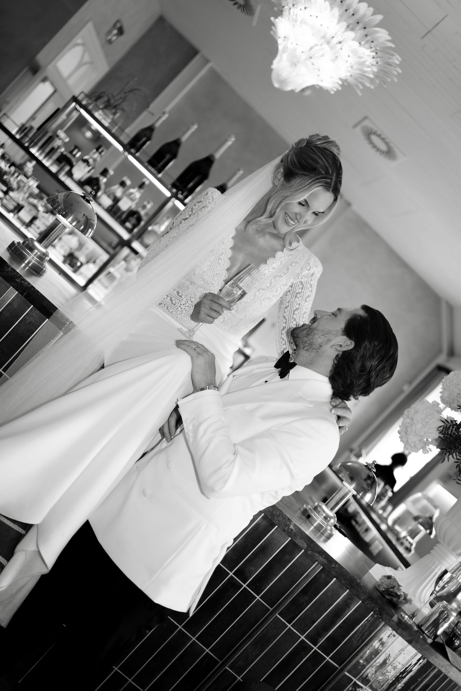 Black and white photo of a smiling bride and groom sharing a romantic moment at their wedding reception bar.