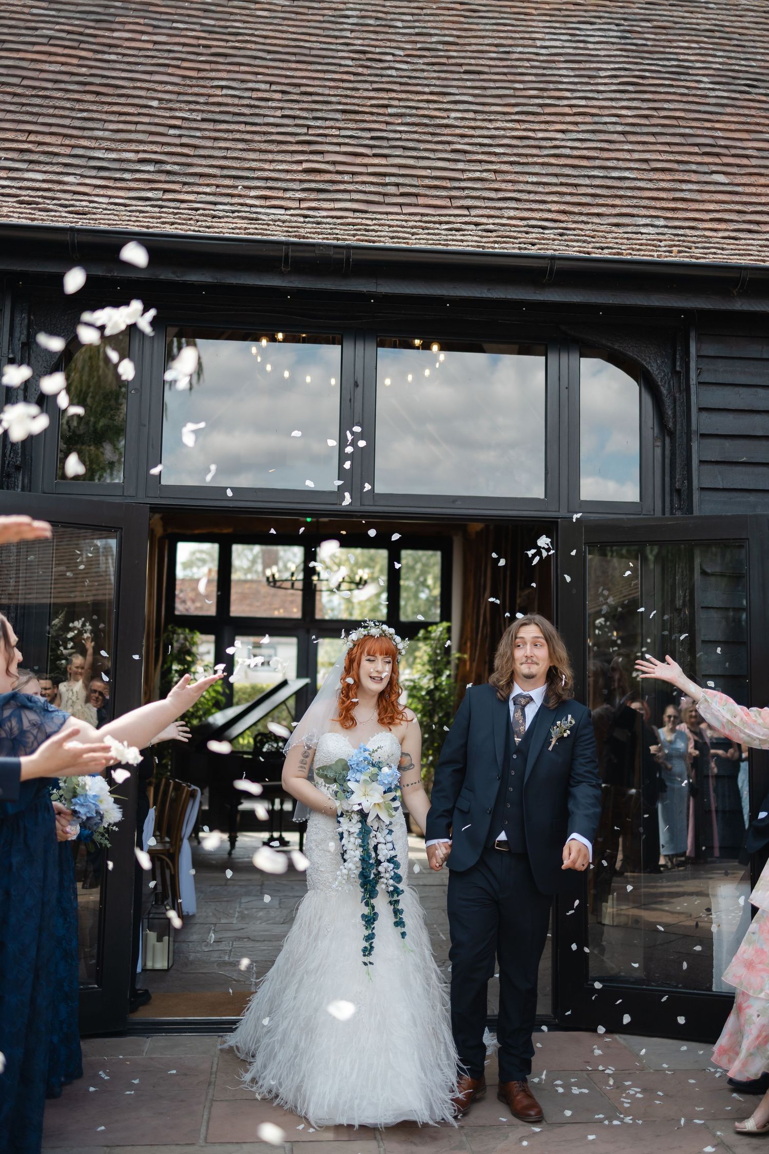 Wedding couple exiting venue under shower of confetti with guests celebrating.