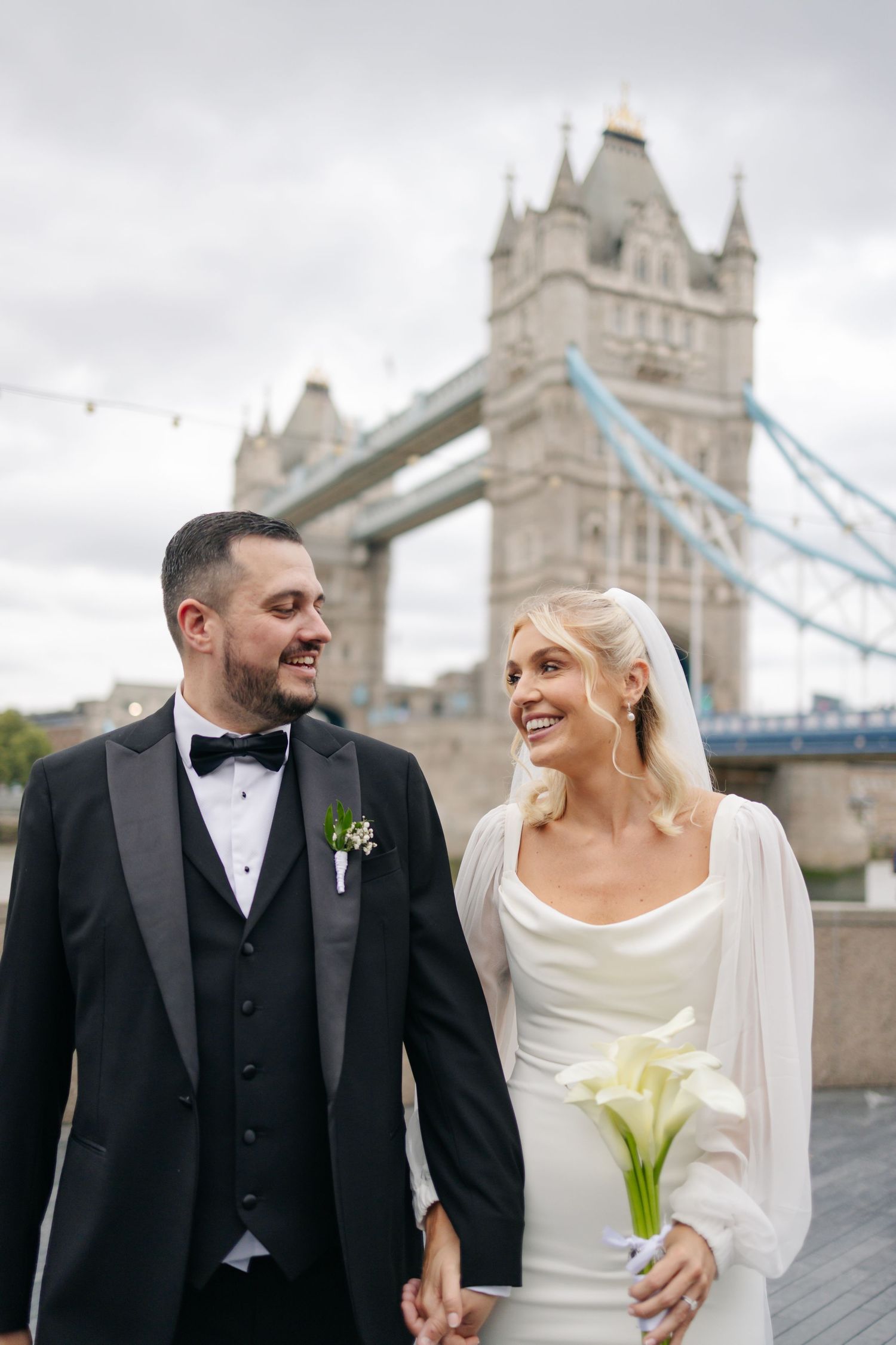 A wedding couple shares joyful moments in front of London's iconic Tower Bridge on their special day.