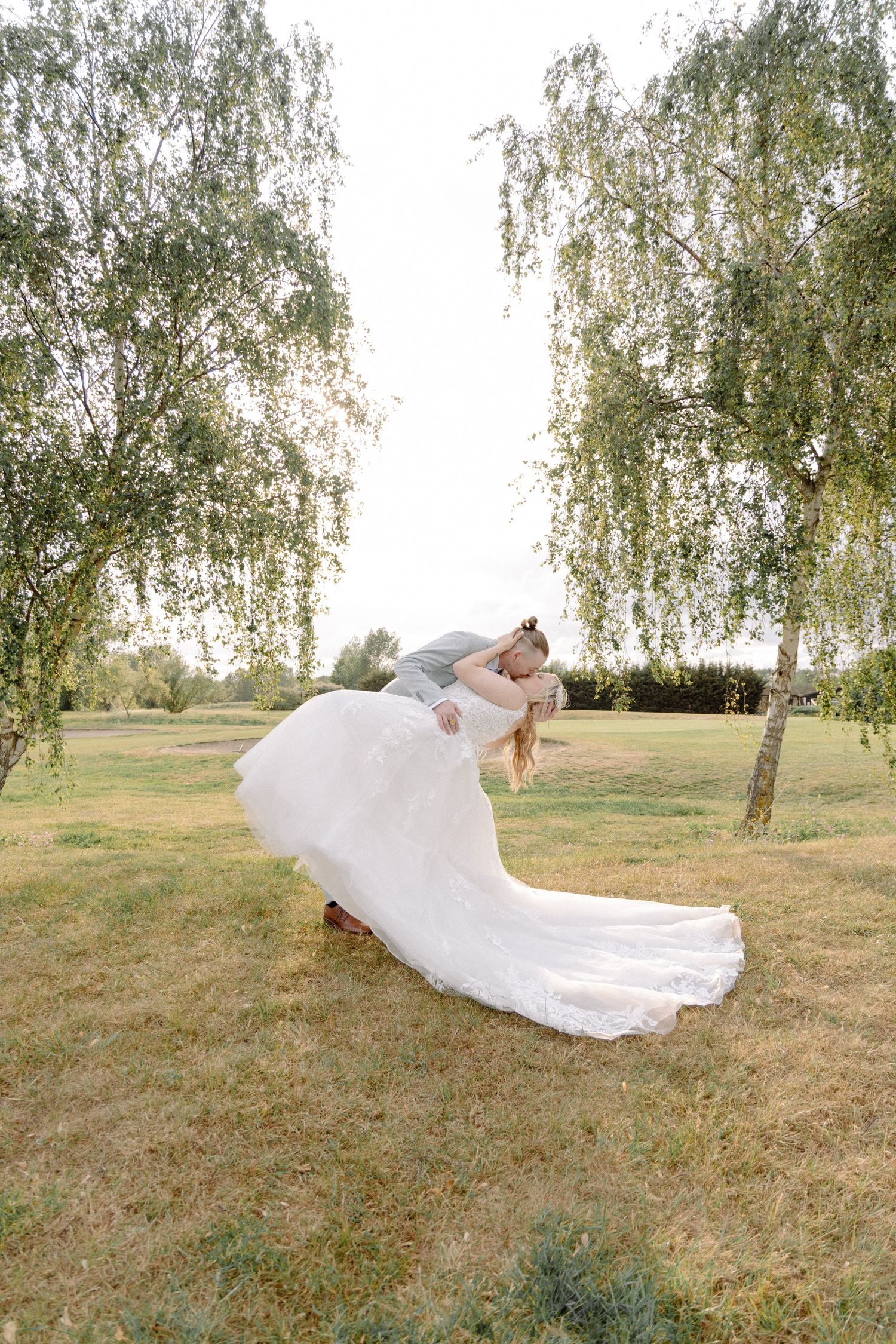 White wedding dress flows dramatically across a grassy hill with birch trees in the background.