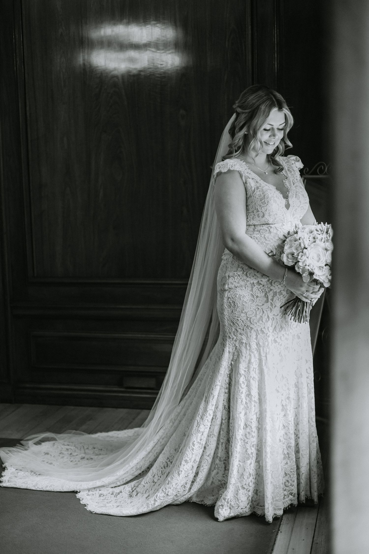 Elegant lace wedding dress with flowing veil captured in dramatic black and white photography.