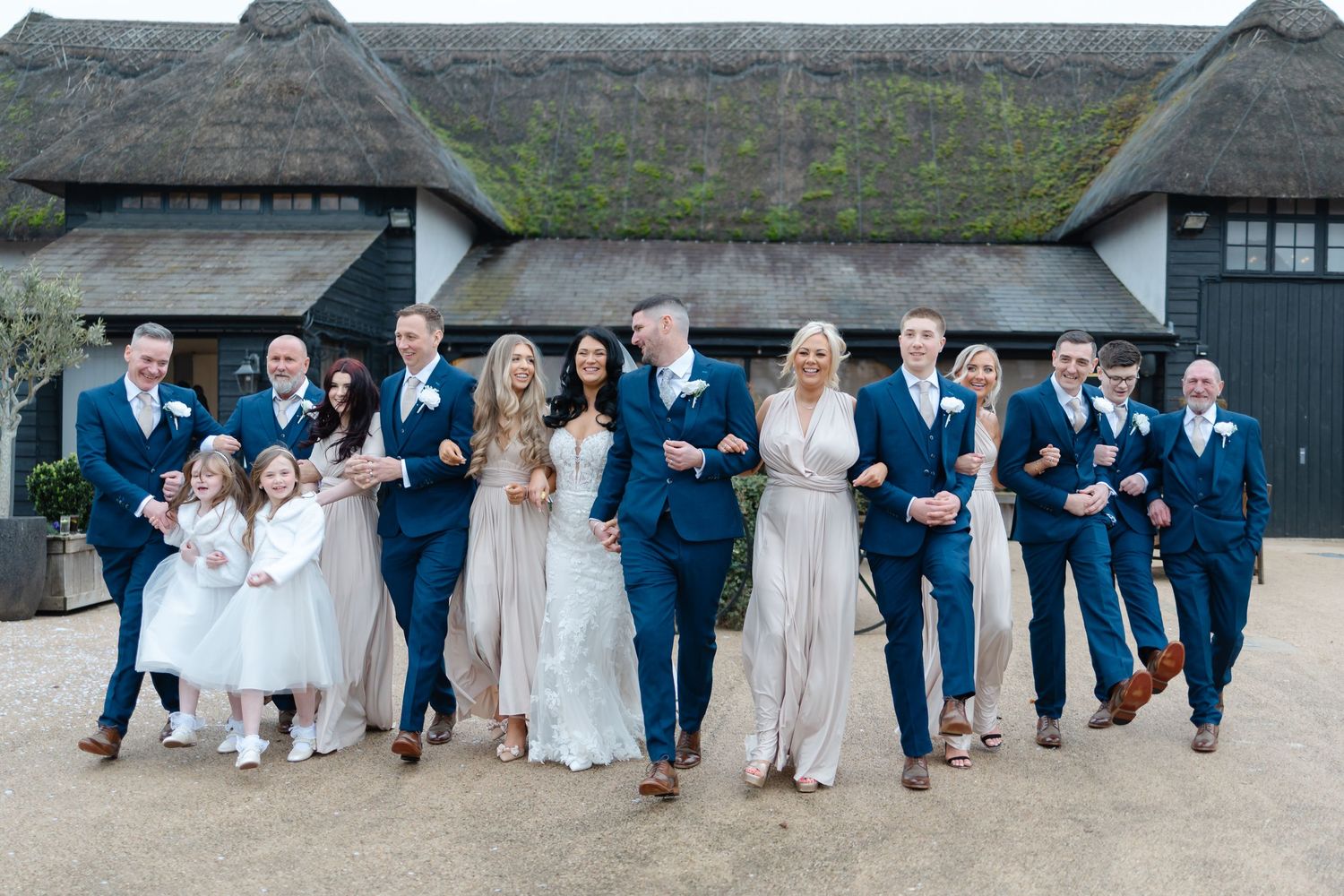 Wedding party members jumping and posing playfully outside a rustic venue.