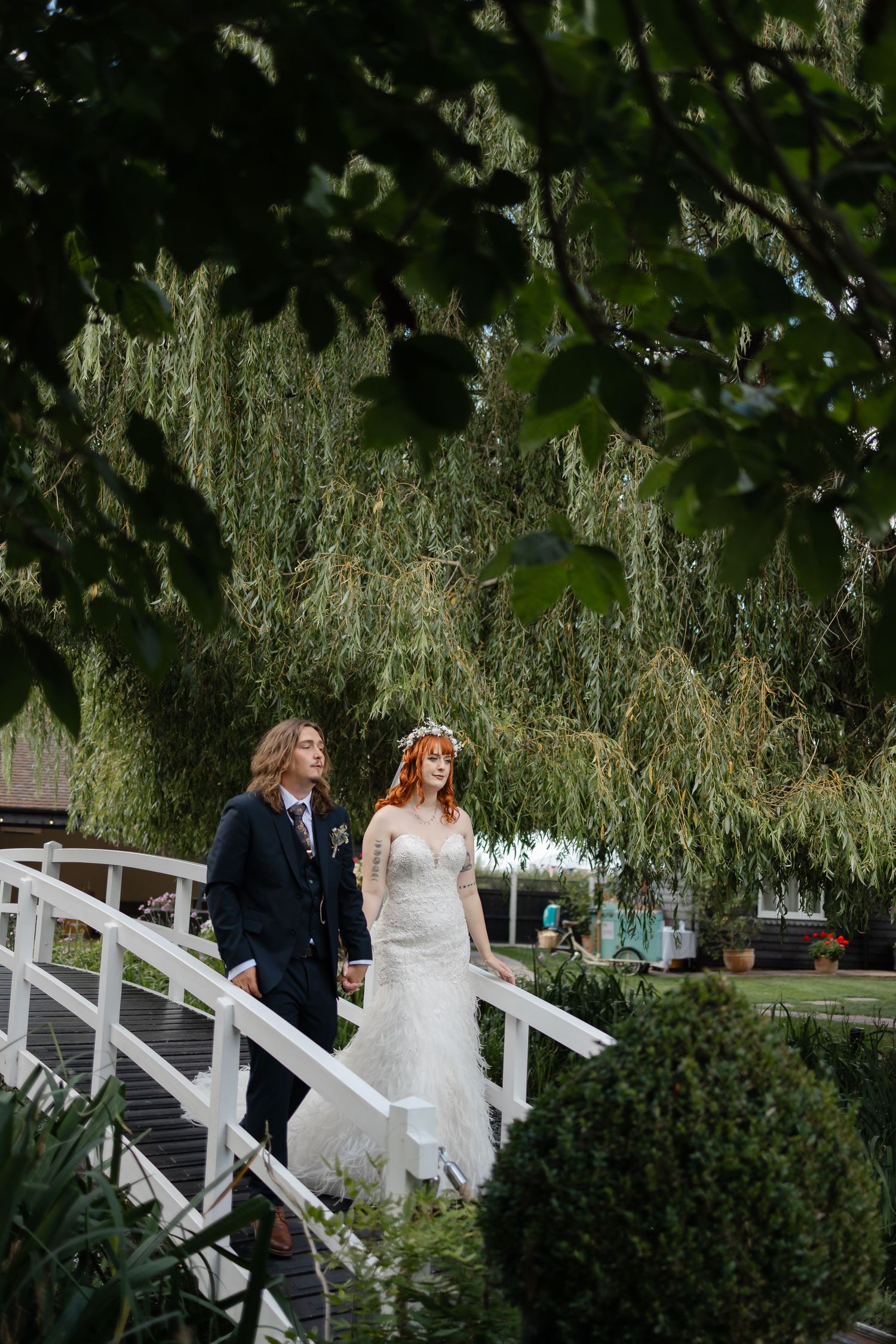 A couple descending a white garden bridge with willow trees in the background.
