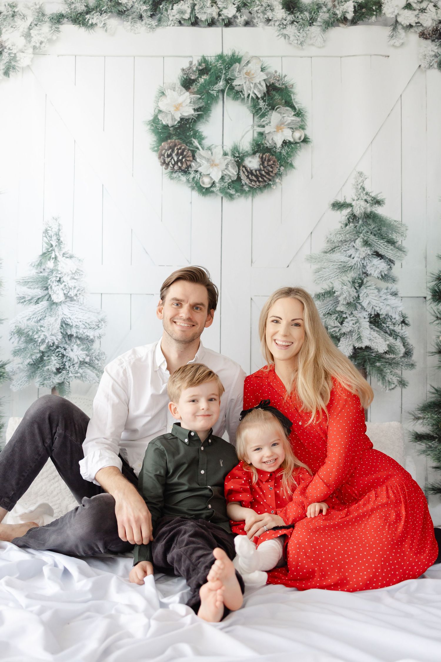 Family holiday portrait with festive winter decor featuring snow-covered trees and a red dress.