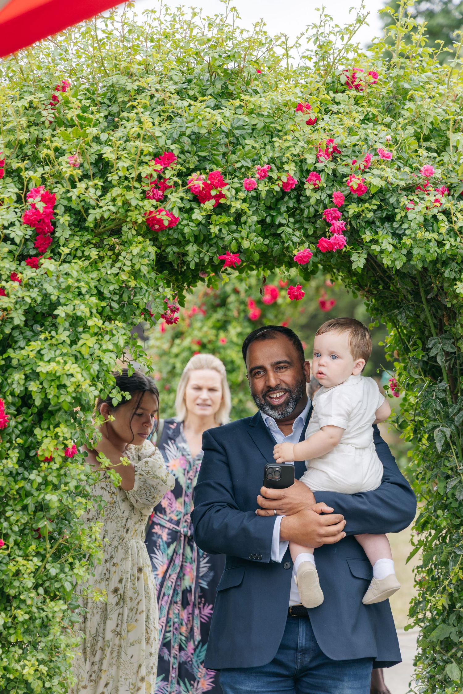 Guests gather under a rose-covered archway during an outdoor celebration.