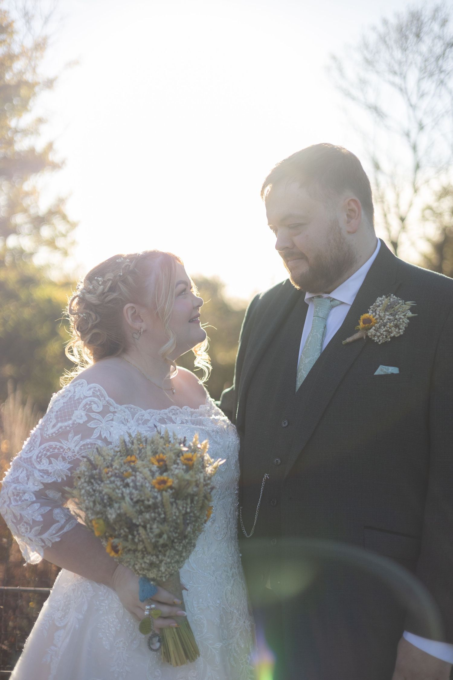 A romantic wedding couple shares intimate moments at sunset with a rustic bouquet of wildflowers.