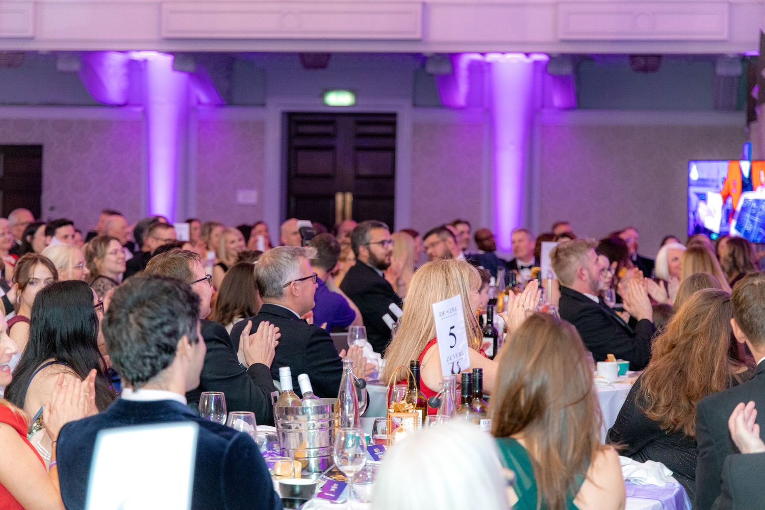 Large crowd gathered in an elegant venue with purple uplighting for a formal celebration.