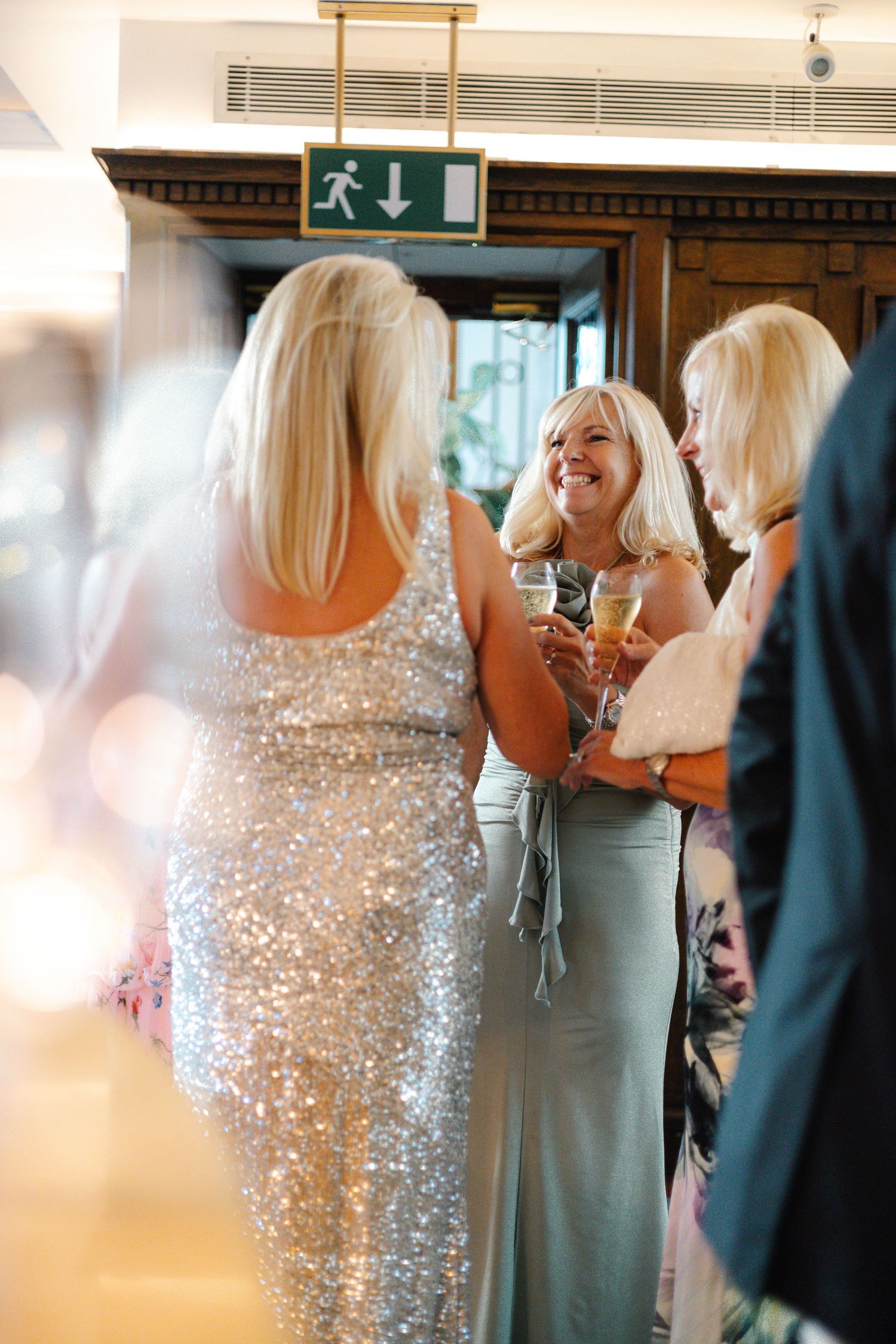 Guests in formal attire mingle at an elegant indoor celebration with sparkly dresses.