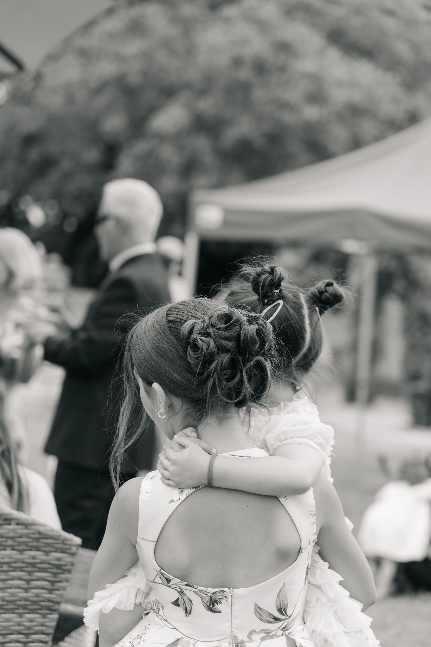 Row of bridesmaids in white dresses shown from behind at an outdoor event.