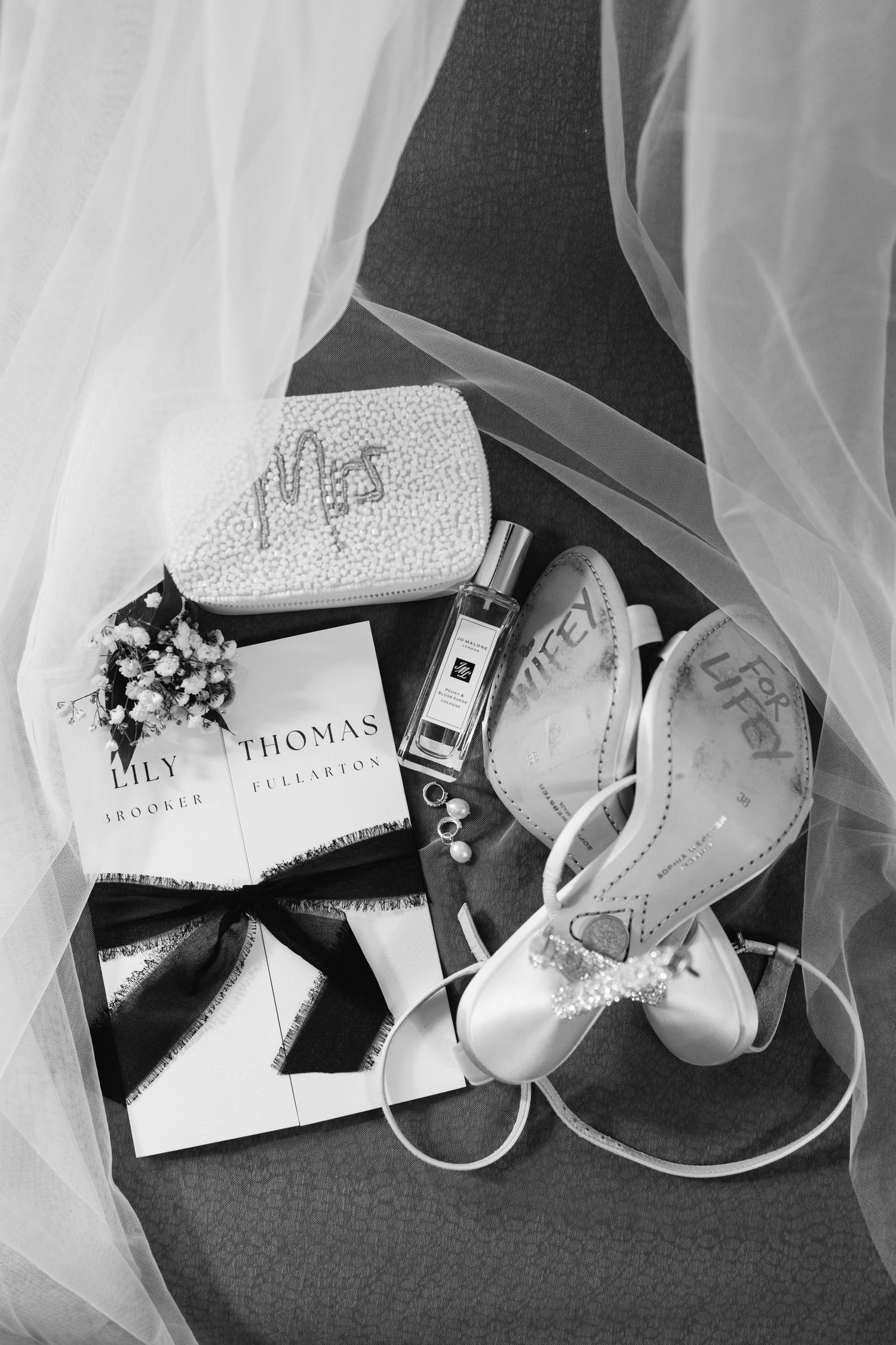 Wedding accessories including white shoes and invitations arranged on dark background.