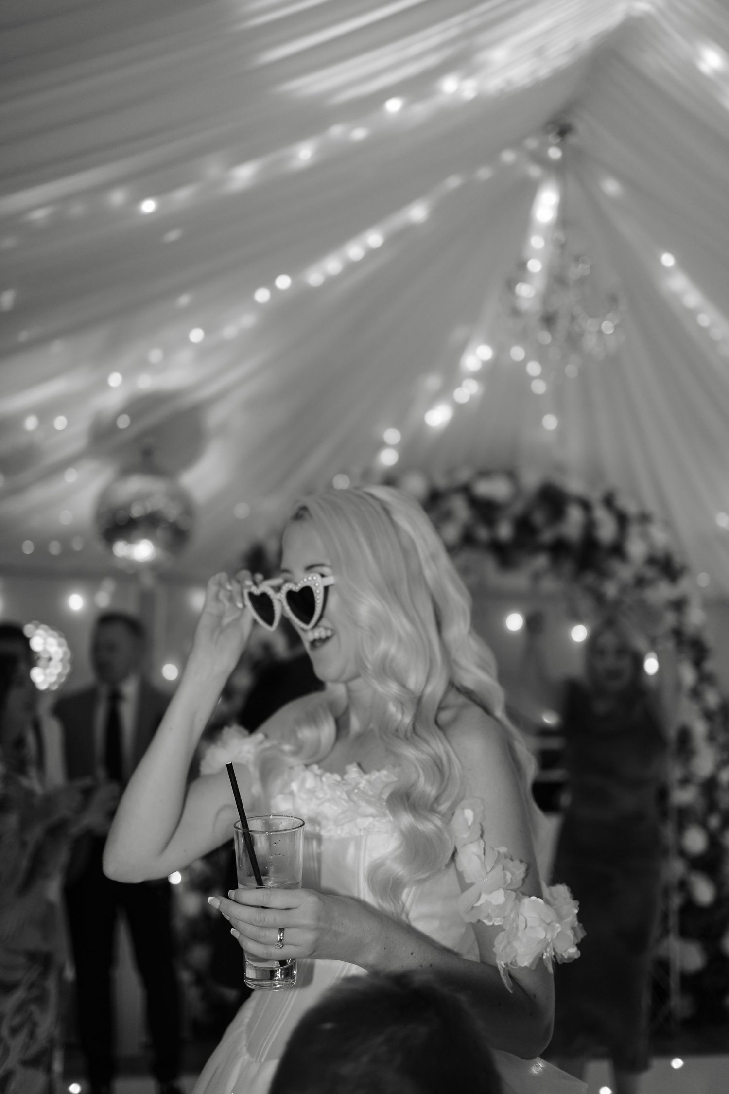 Black and white reception photo showing dancing and celebration under draped ceiling with twinkle lights.