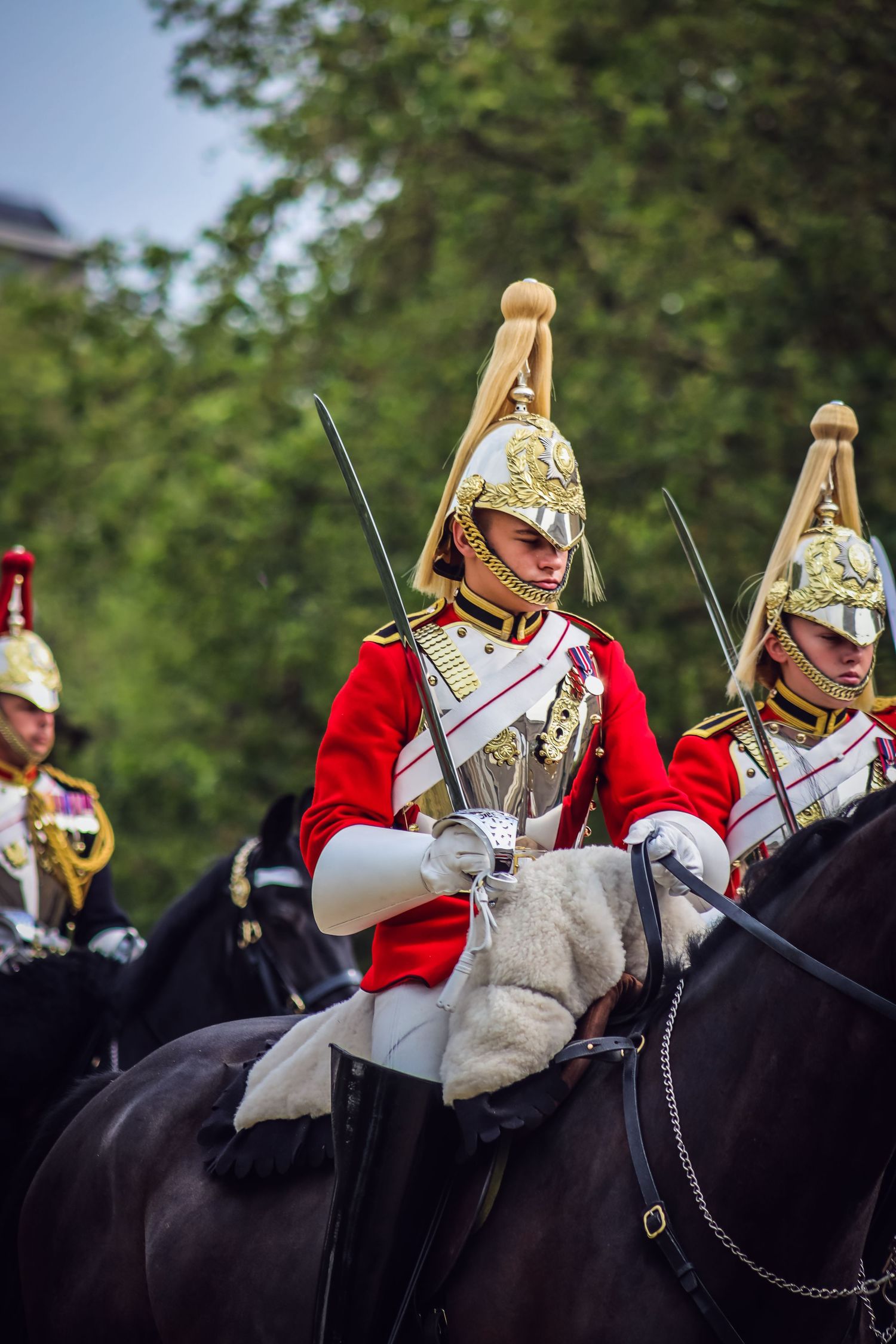 Mounted cavalry soldiers in ceremonial dress uniforms with gold helmets and red coats.