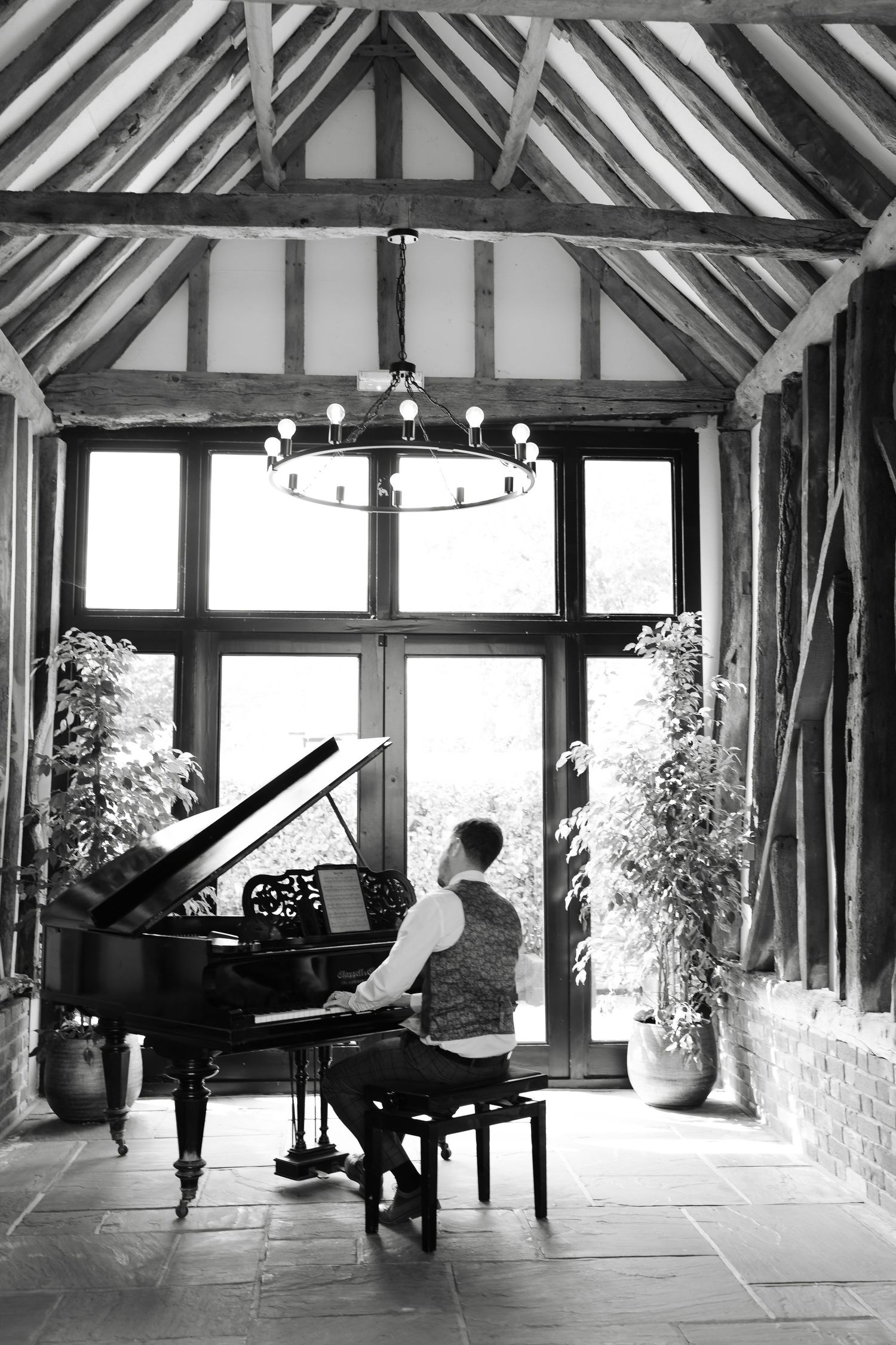Black and white photos of a grand piano in a rustic timber-framed room with vaulted ceiling.