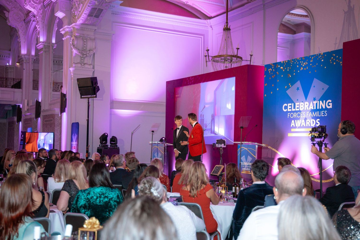 Wide view of an awards ceremony stage with purple lighting and celebration banner.