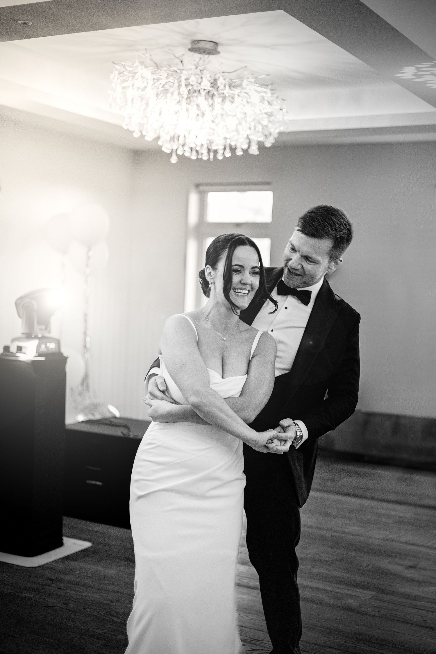A couple shares a playful dance moment under an elegant crystal chandelier.