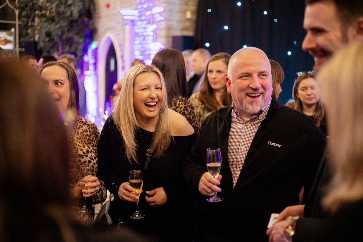 Event guests enjoying drinks and conversation in a dimly lit venue with purple accent lighting.