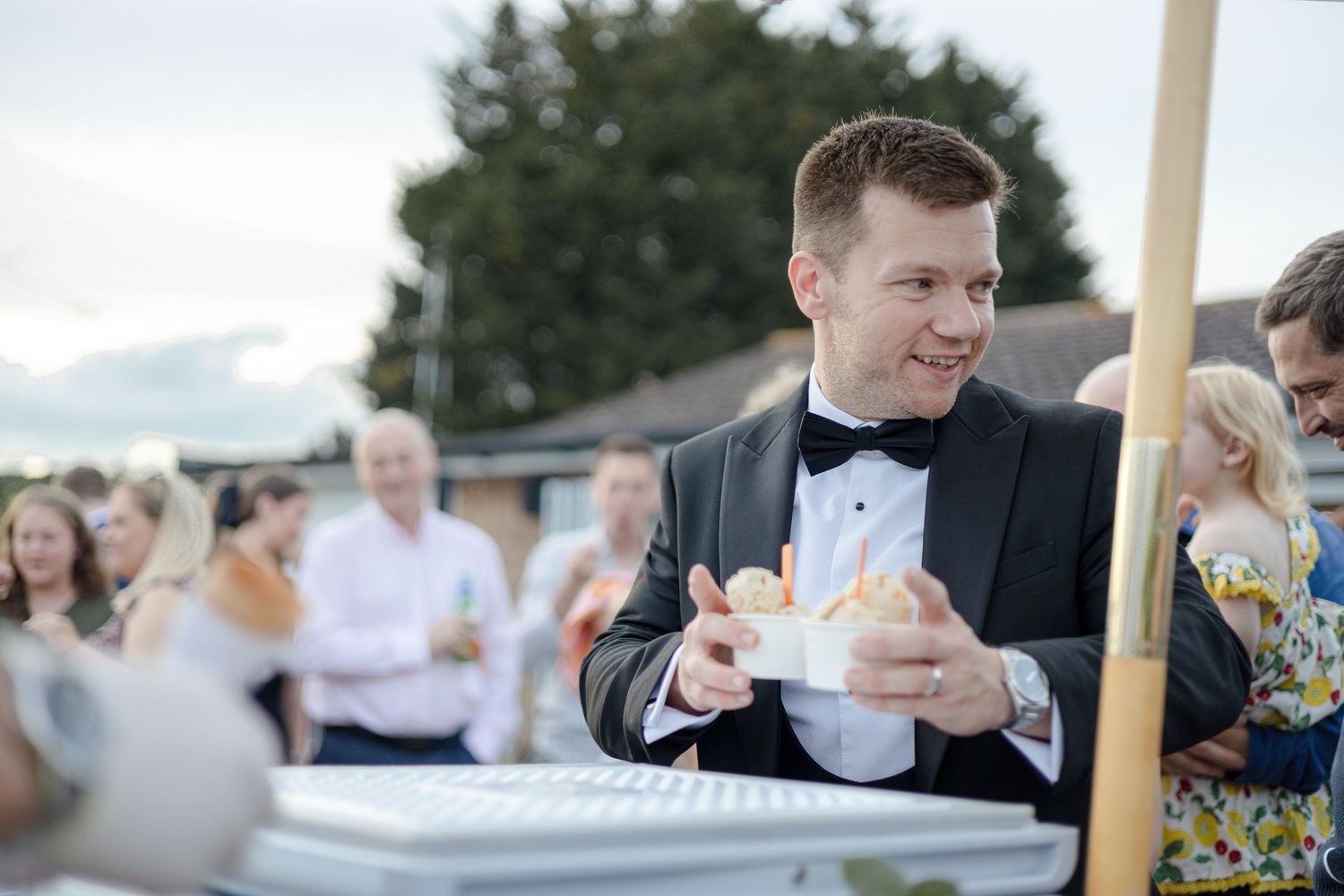 Guest in formal attire enjoys refreshments at an outdoor celebration.
