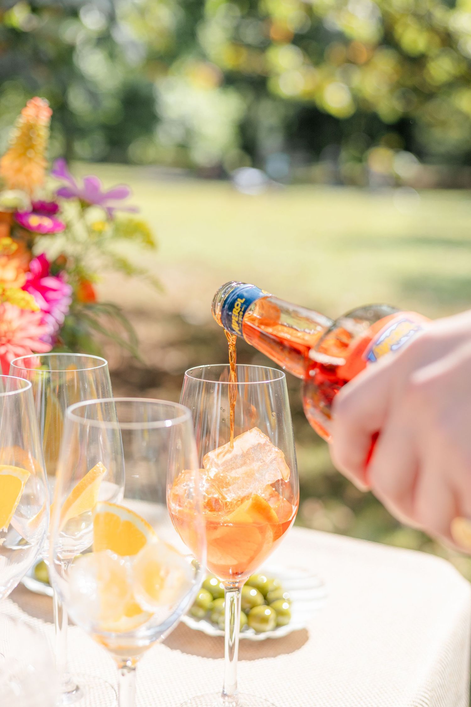 Champagne being poured into glasses at an outdoor event with colorful flowers.
