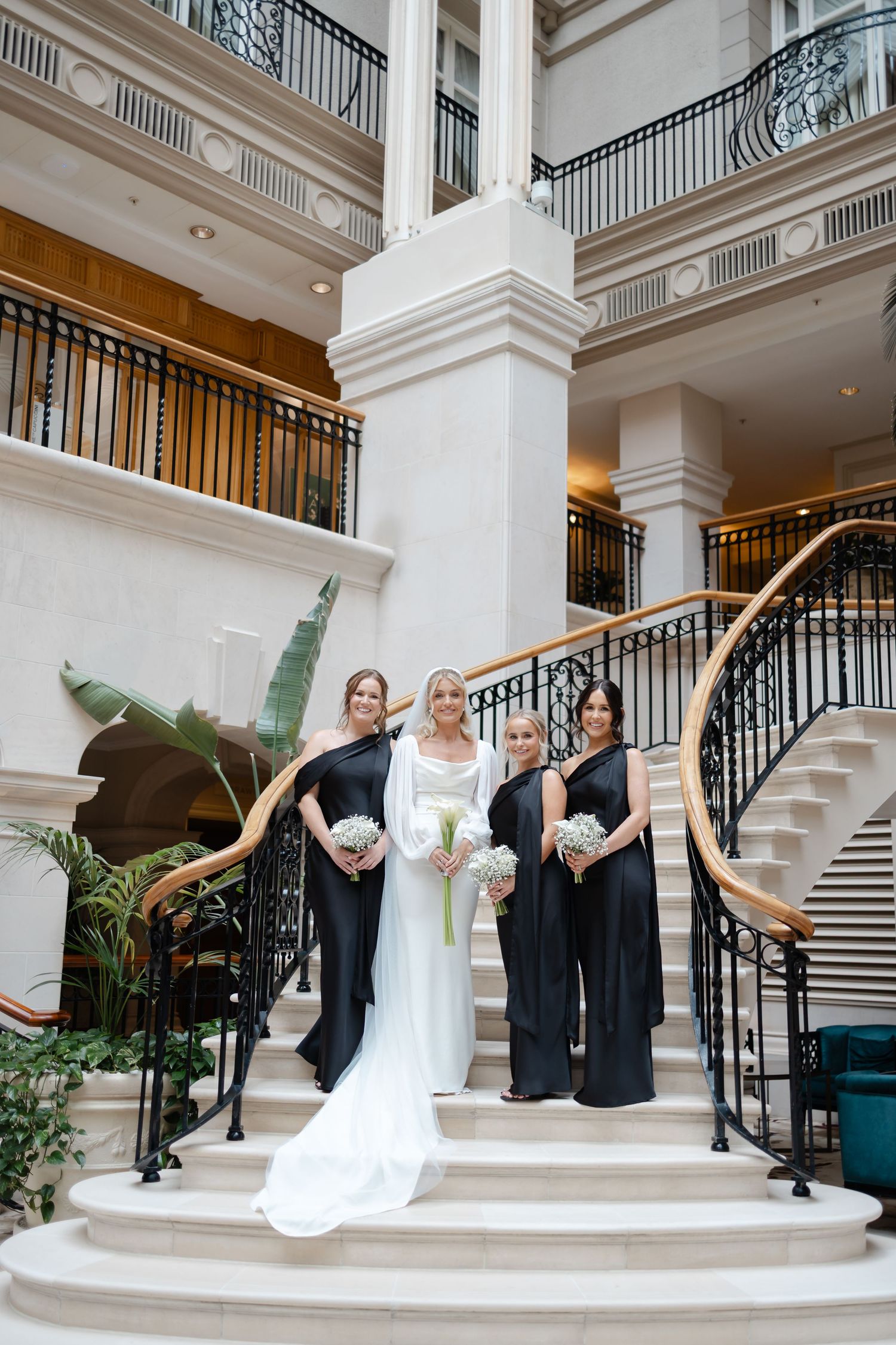Wedding party poses on grand white marble stairs with bridesmaids in navy dresses.