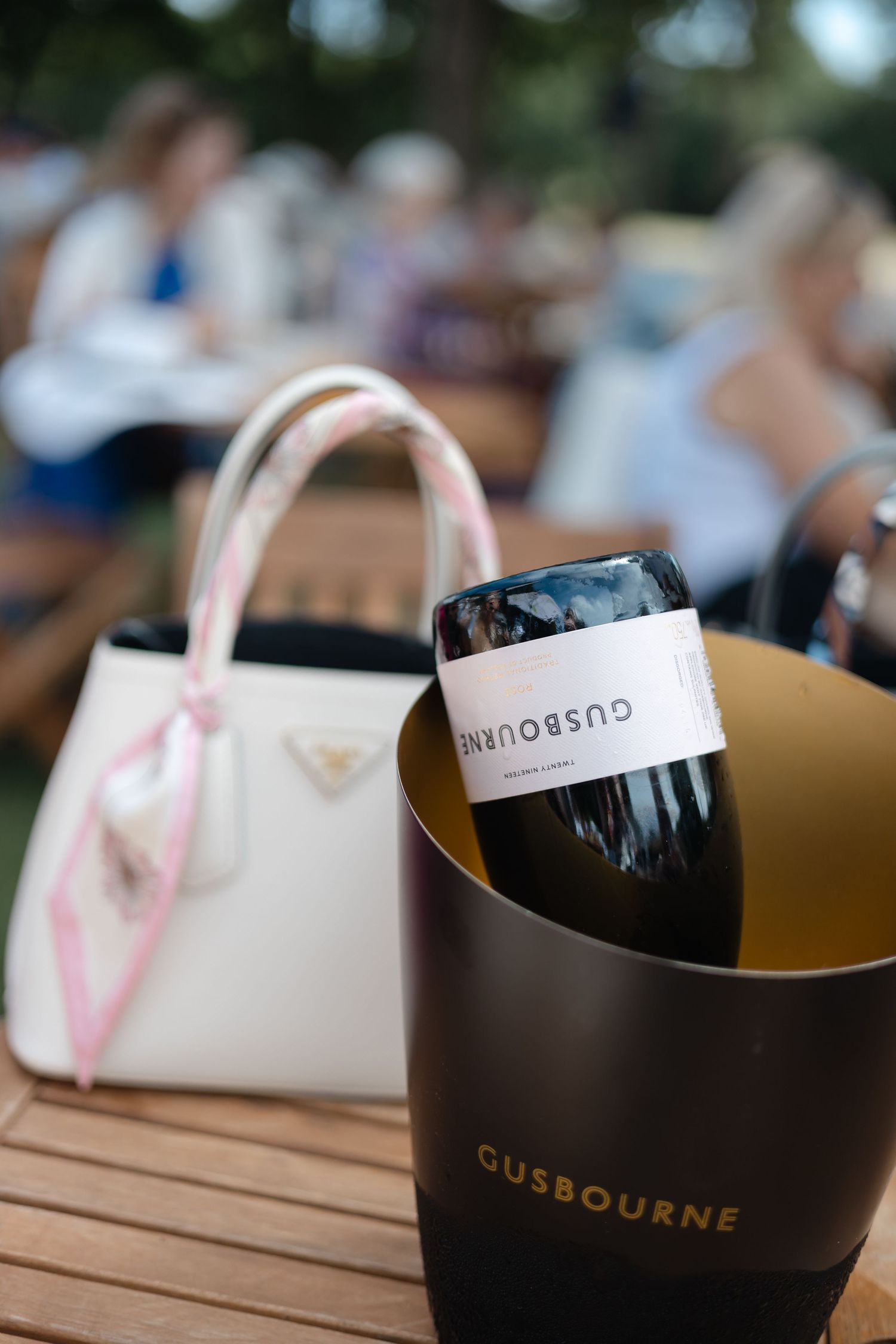 Row of branded gift bags arranged on wooden outdoor table.