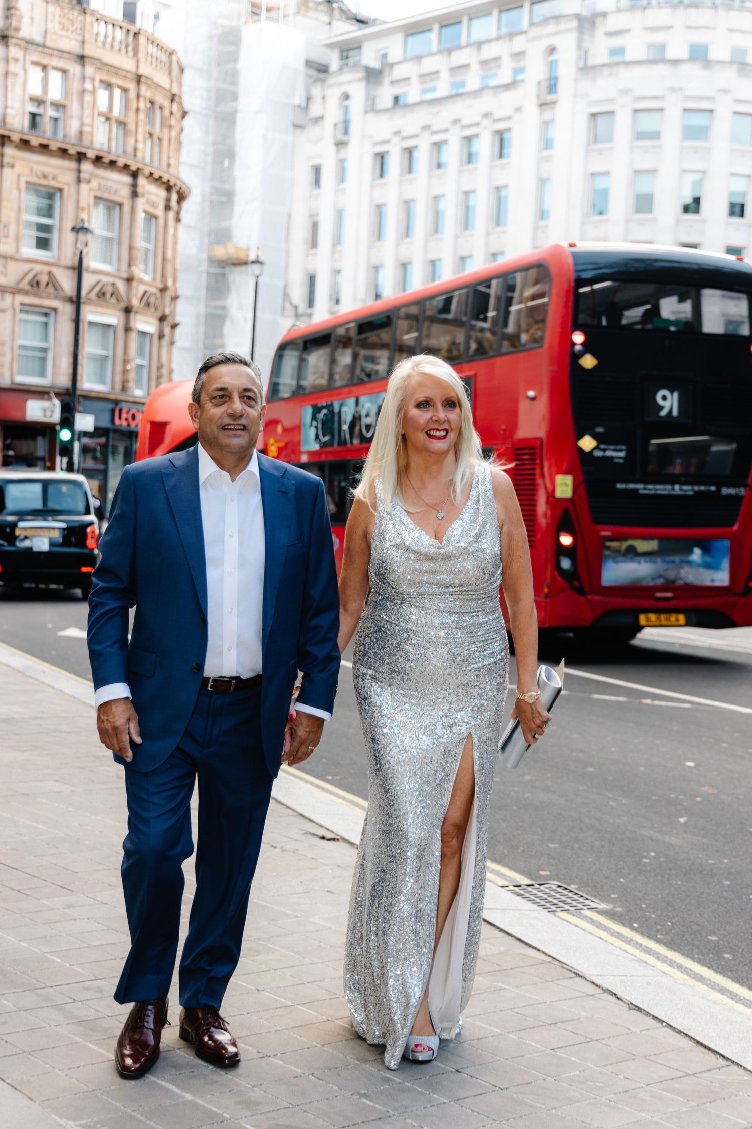 Couple walking along a London street with red double-decker buses in the background.