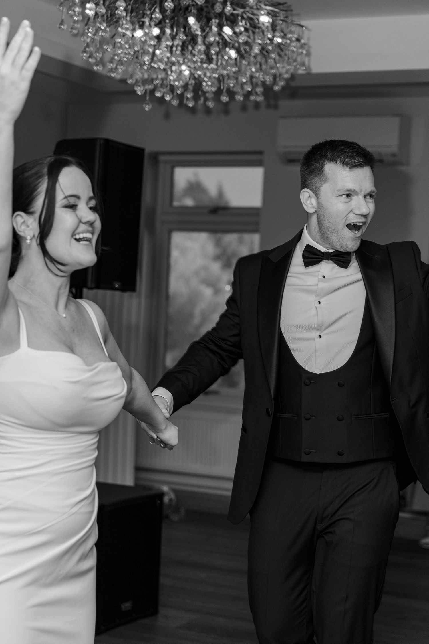 Wedding party dancing and celebrating under crystal chandeliers in black and white.
