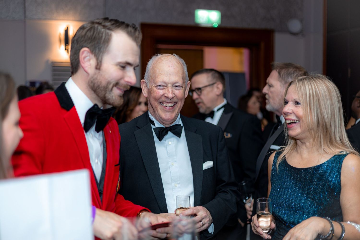 Formal party guests gather for conversation and drinks under soft lighting.