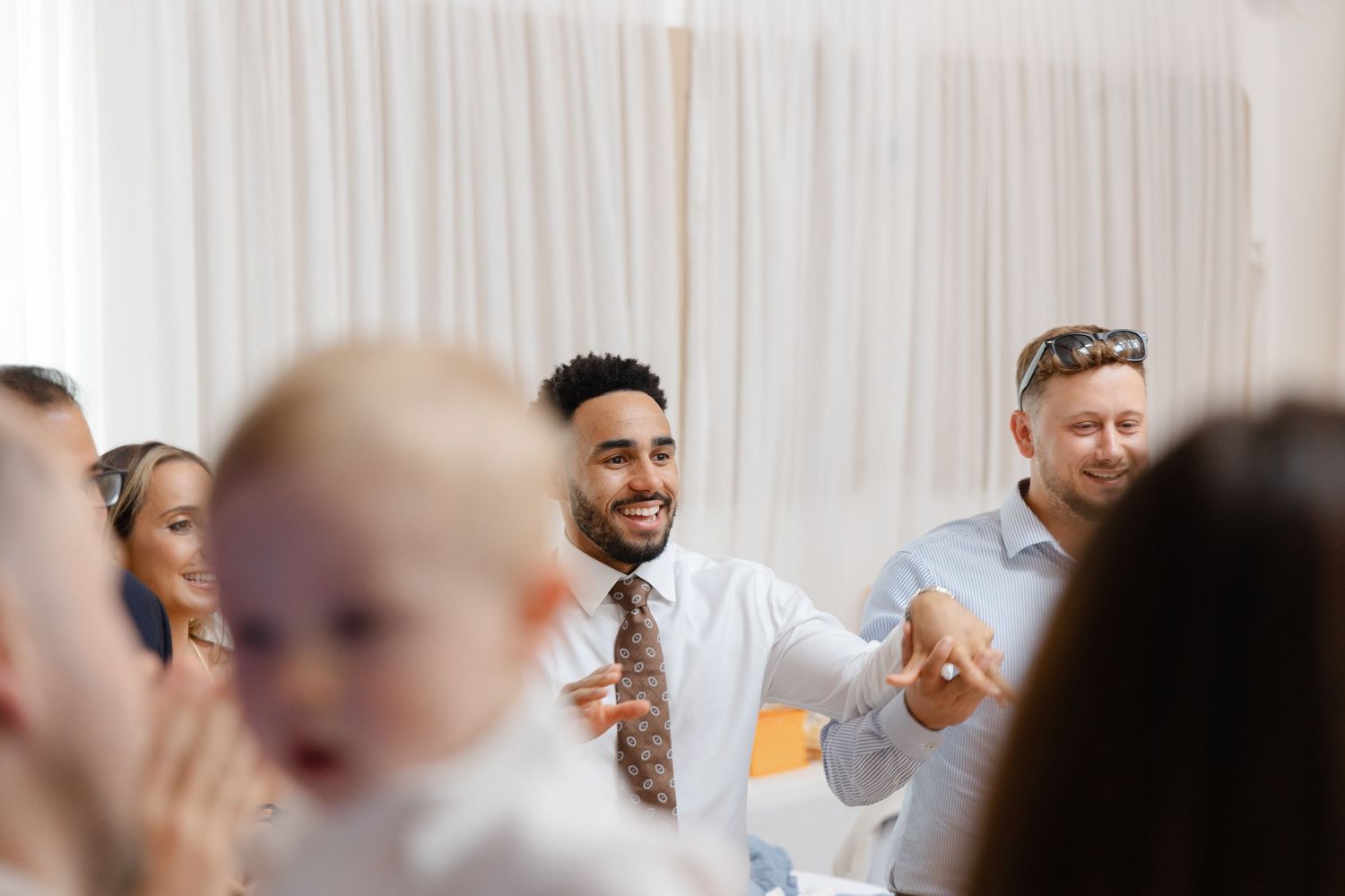 Guests enjoying themselves at an indoor celebration with white drapes in the background.