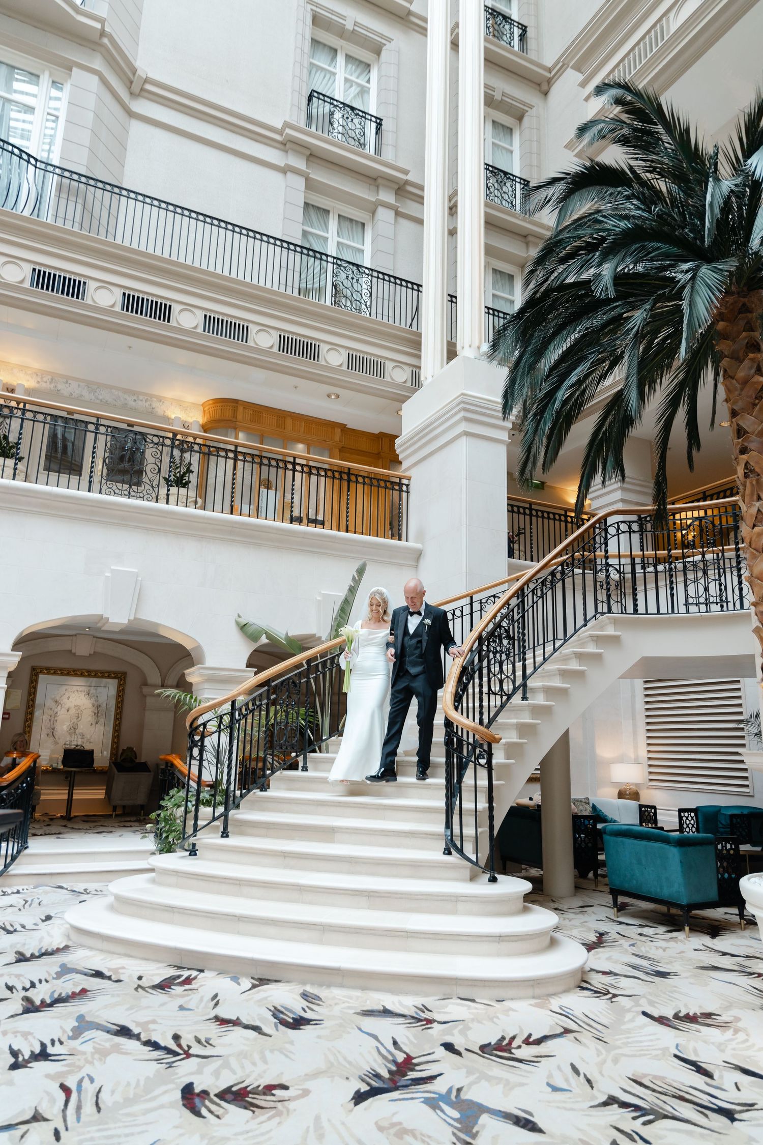 Grand white marble staircase with palm trees in luxury hotel lobby.