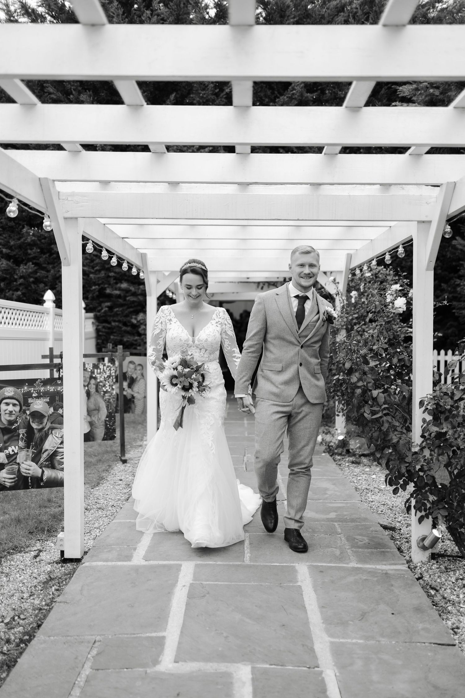 Couple walking under white garden pergola during wedding ceremony.