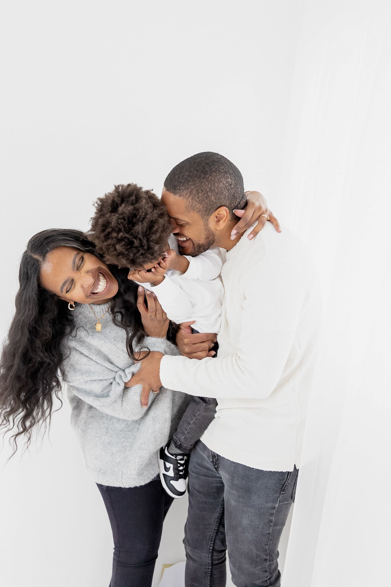A family plays and laughs together while wearing casual clothing against a white backdrop.