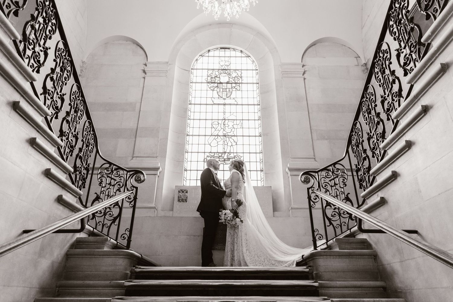 Dramatic wide-angle view of an elegant staircase with ornate iron railings and arched windows.