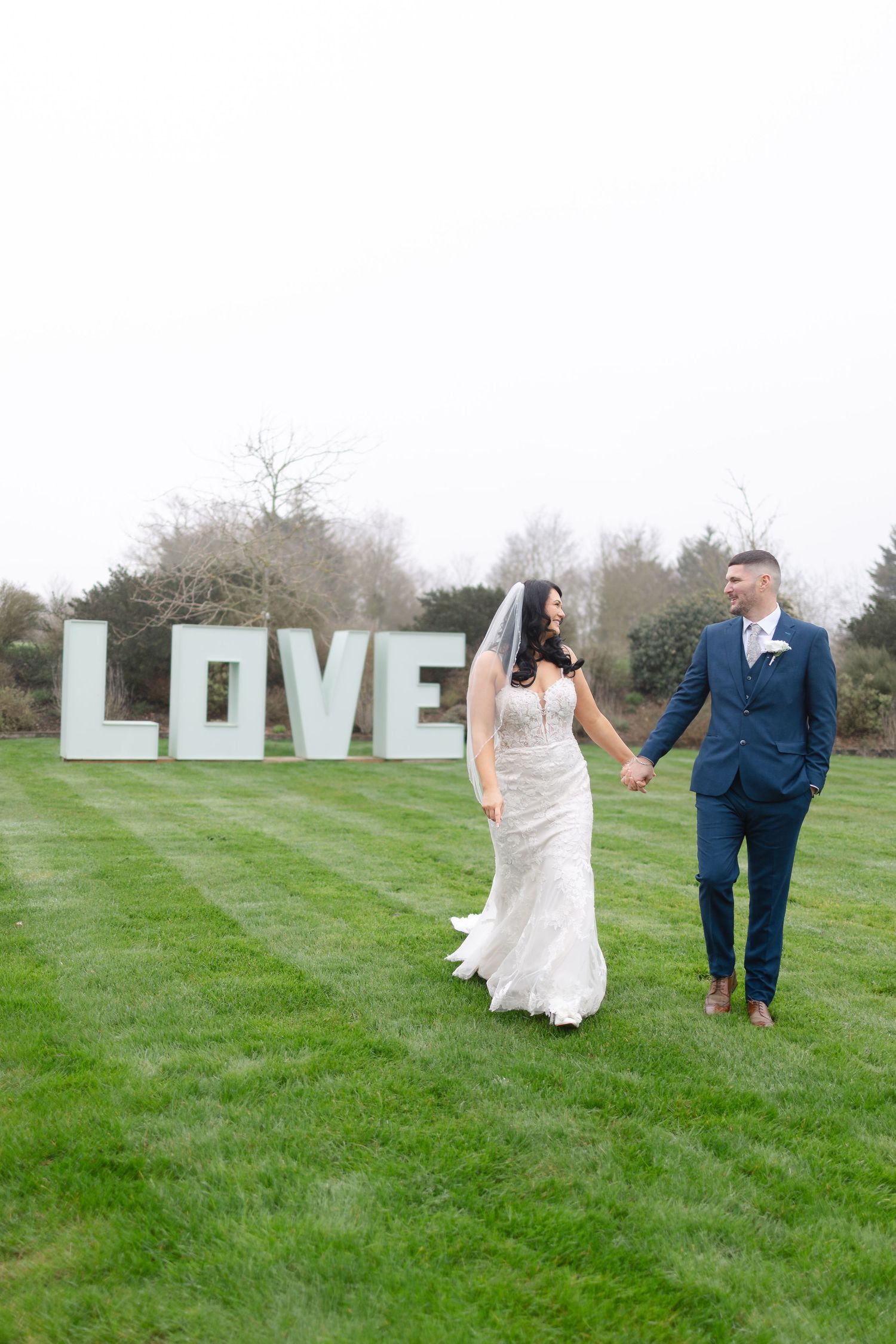Wedding couple walking through a field with large white LOVE letters in the background.
