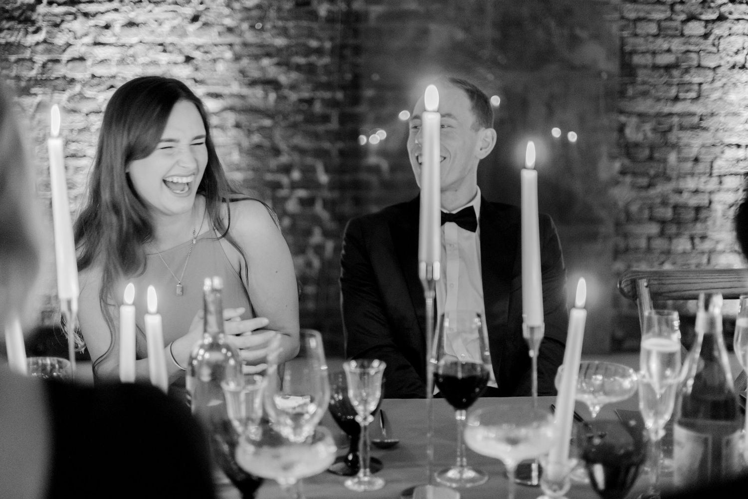 Joyful dinner conversation around a candlelit table with wine glasses and brick wall ambiance.