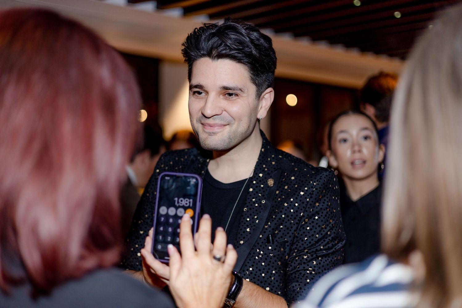 Person in sparkly black shirt posing for photos with mobile phones at a social event.