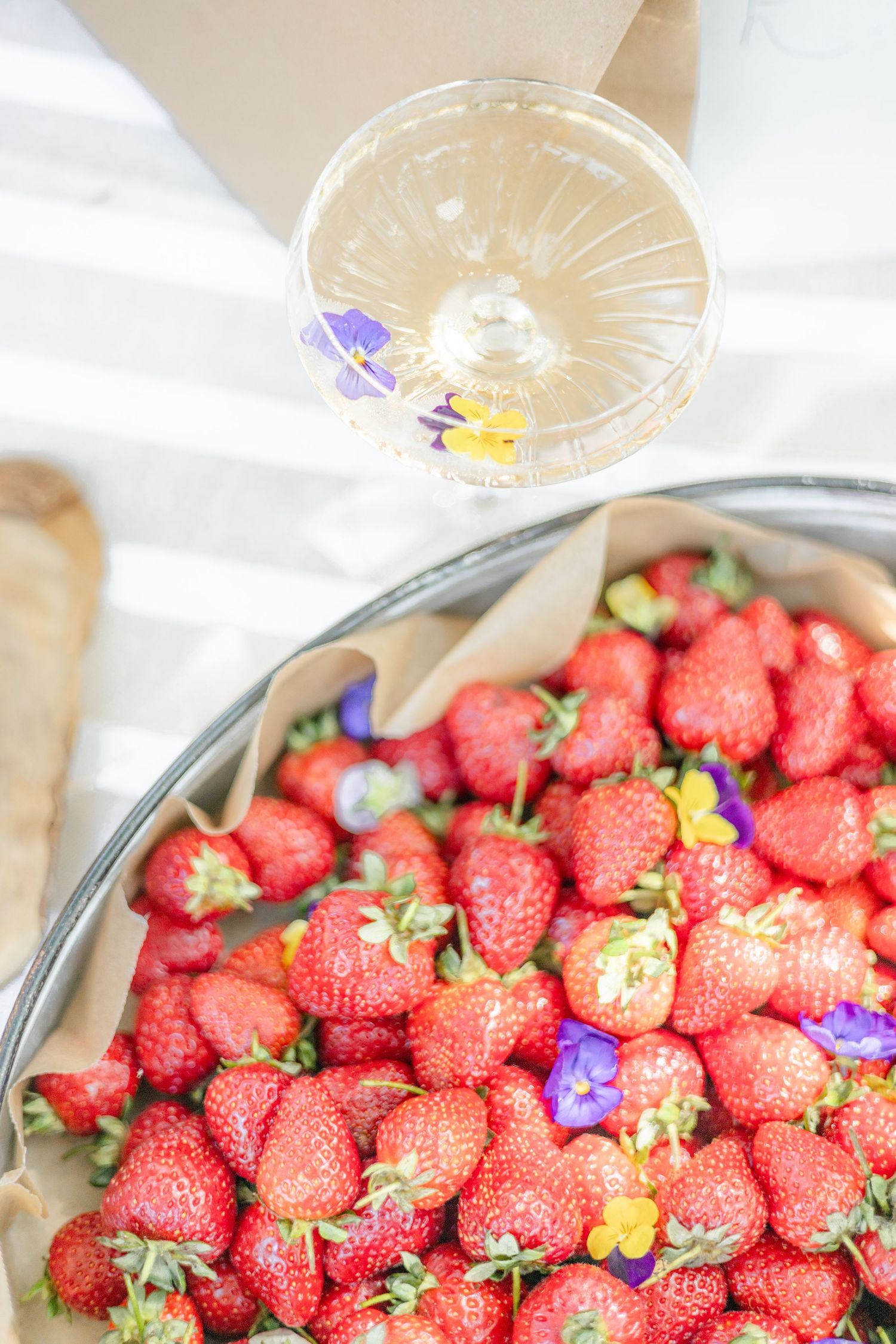 Fresh red strawberries garnished with purple edible flowers in a serving dish.